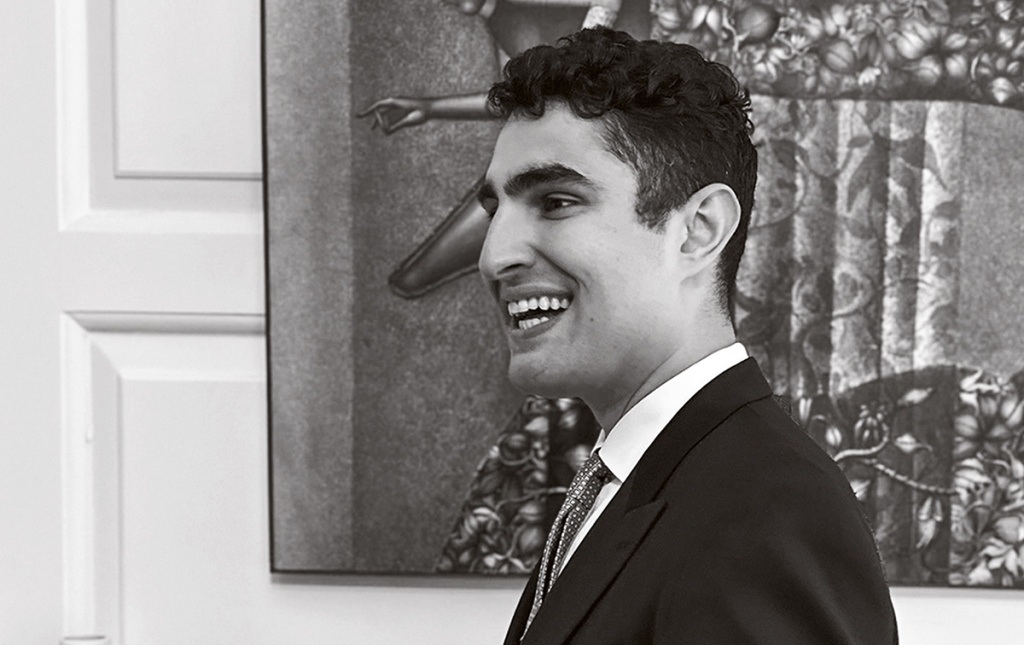 B+W image of Ben Shields smiling with a painting behind him.