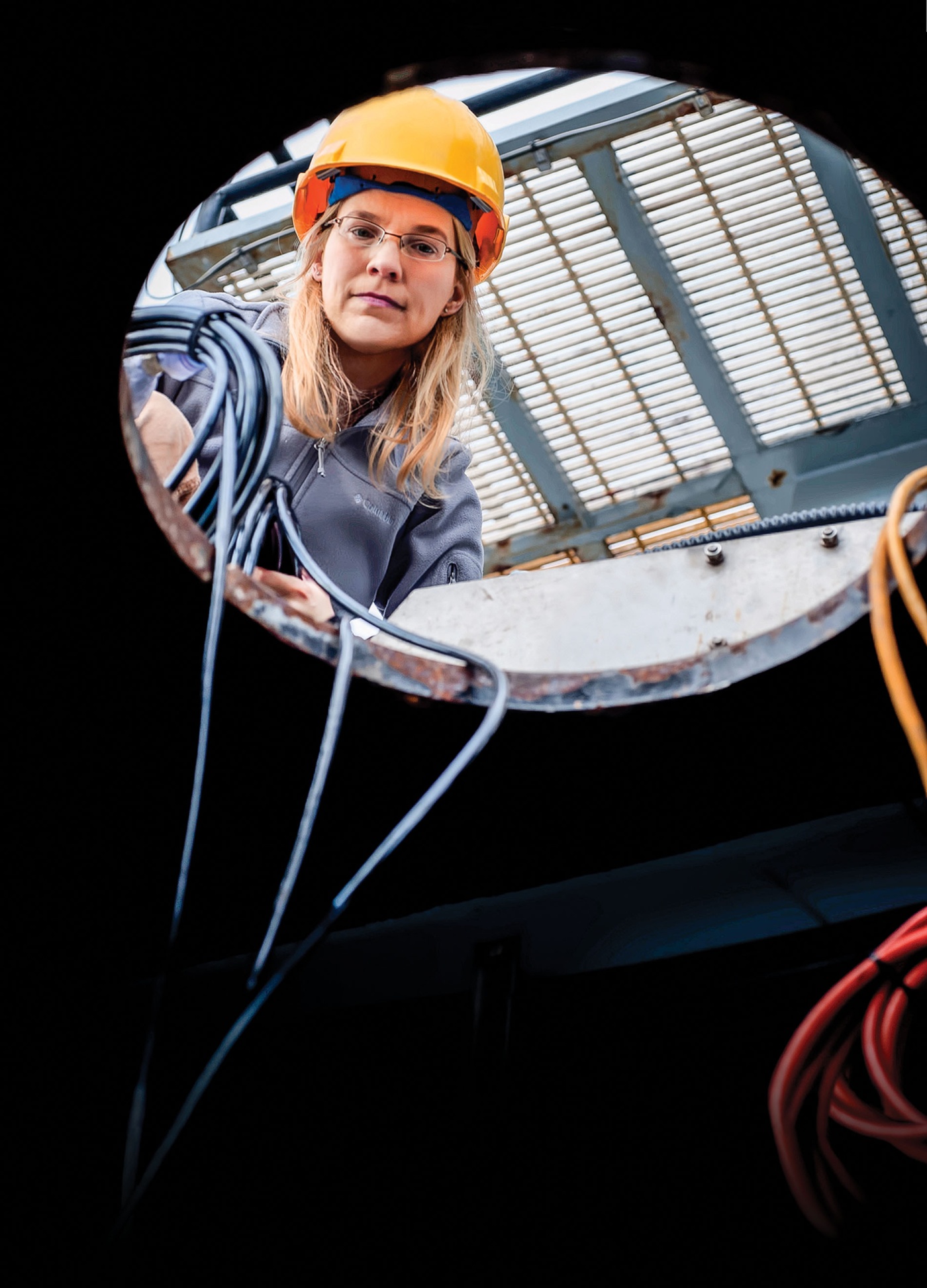 Image of Kelly Benoit-Bird looking down a manhole with a hard hat on.