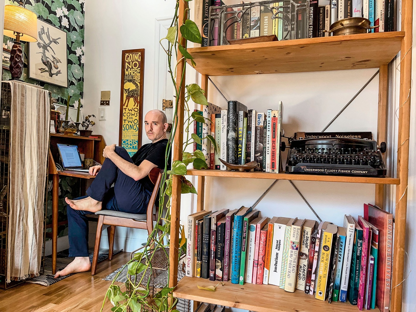 Image of Jonathan Corcoran sitting in a chair with a bookshelf in the foreground.