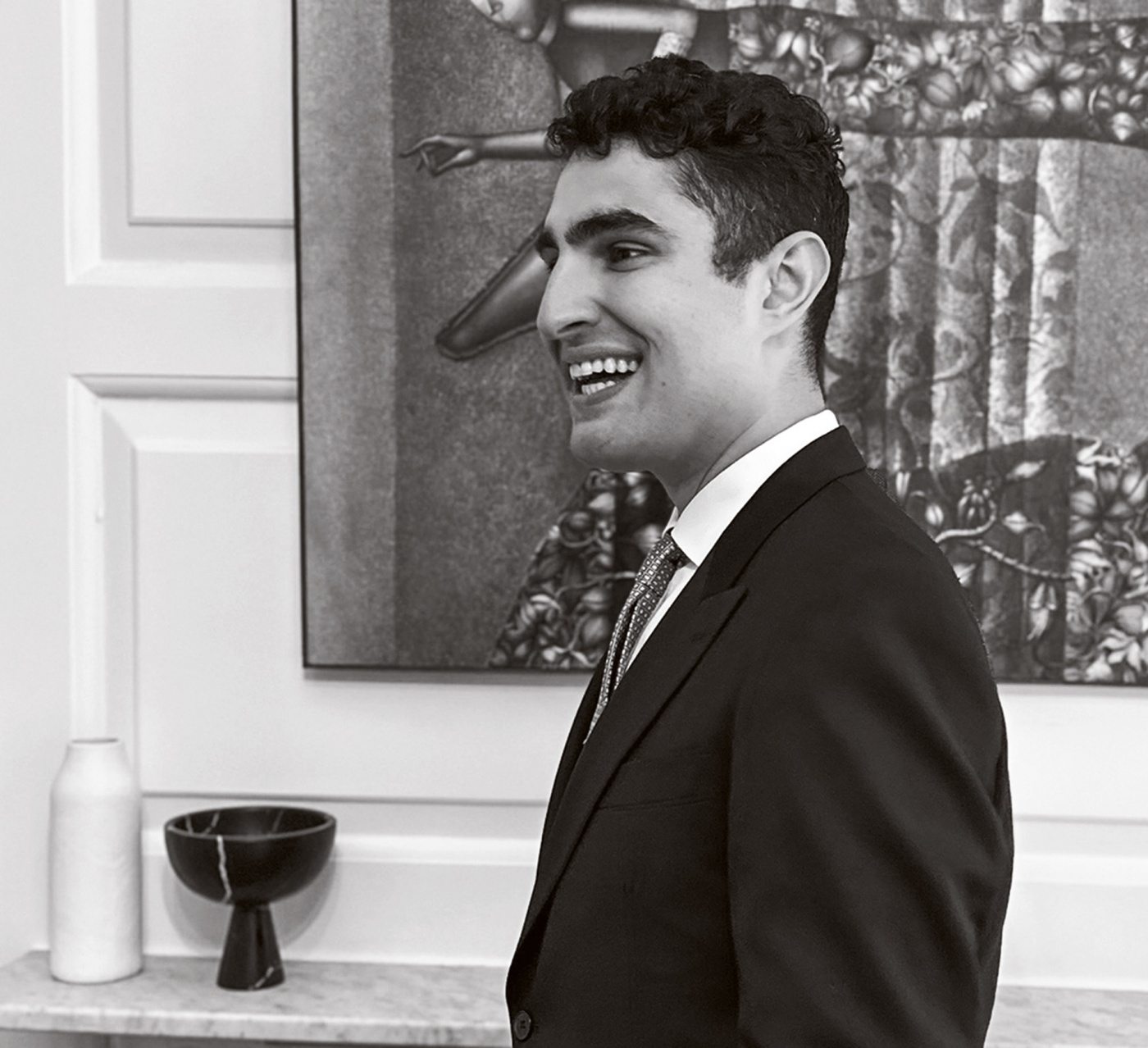 B+W image of Ben Shields smiling with a painting behind him.