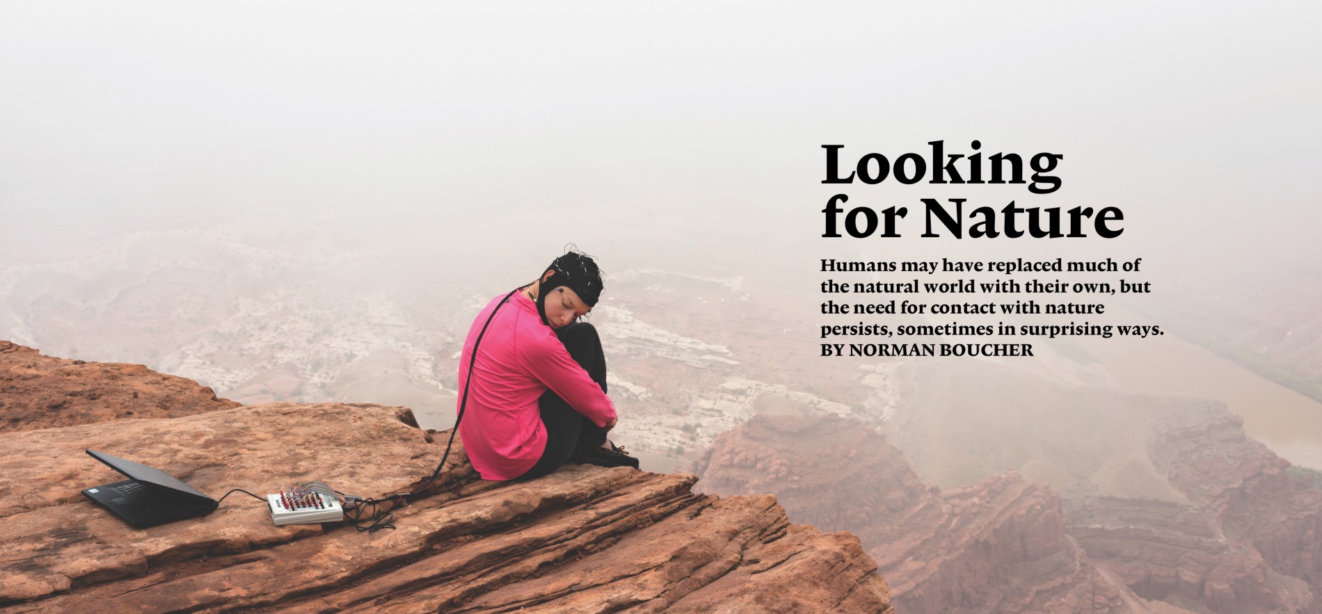 Woman sits on the edge of a cliff, wearing an electrical cap attached by a cord to a laptop computer