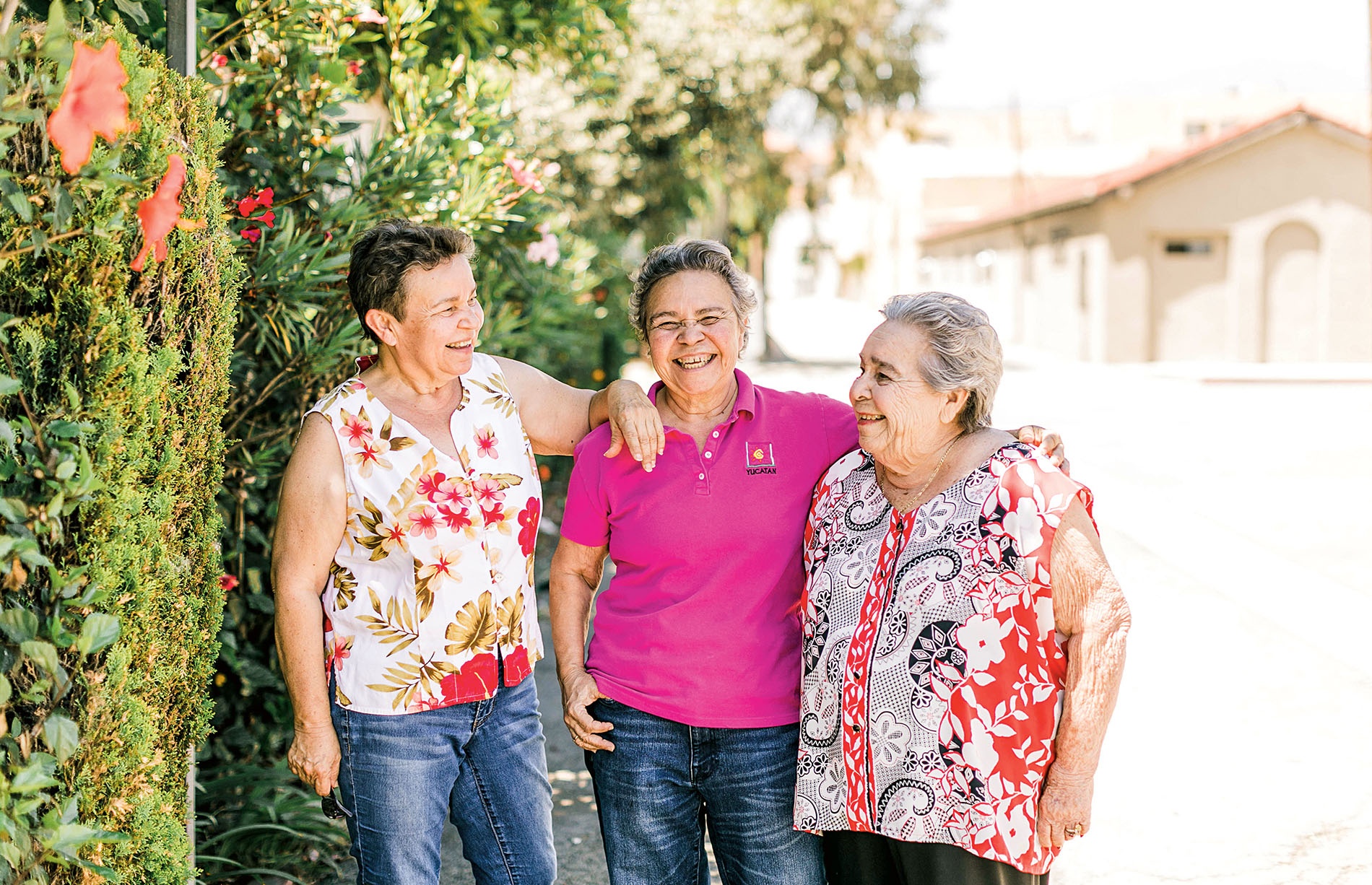 Three women standing in front of a botanical wall smiling. 