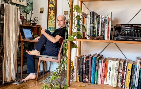 Image of Jonathan Corcoran sitting in a chair with a bookshelf in the foreground.