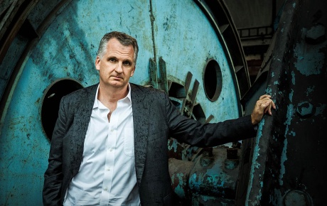 Image of Timothy Snyder standing with an old defunct factory wheel behind him.