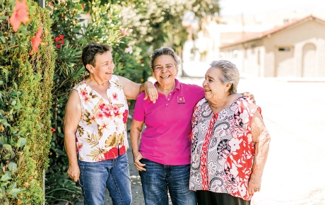 Three women standing in front of a botanical wall smiling. 